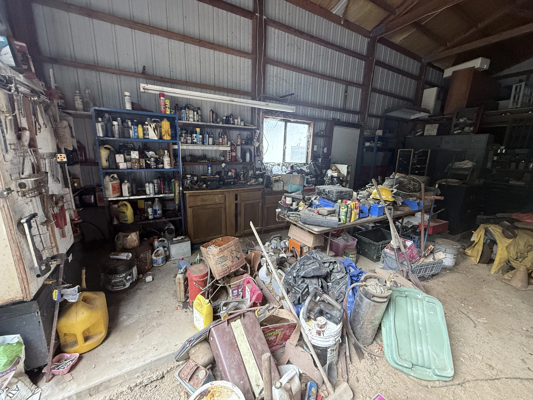 The metal-sided barn before cleanup, with shelving, tools, and equipment across the floor