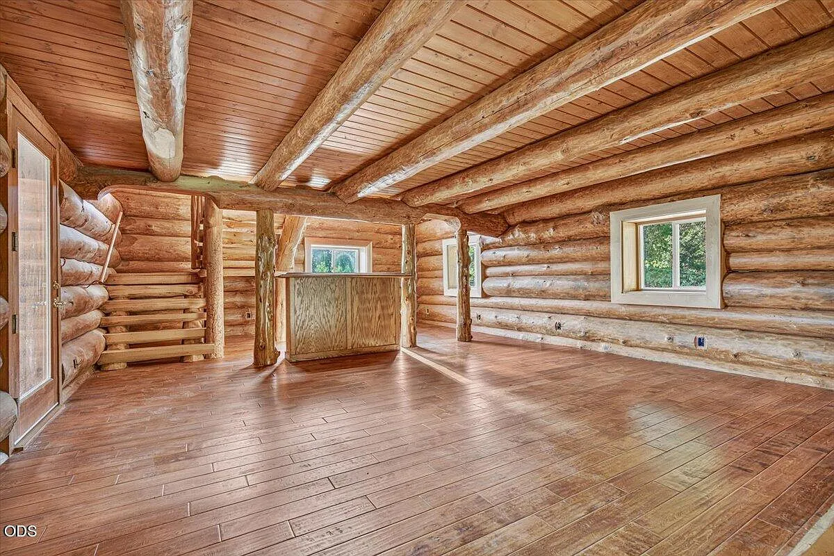 The log cabin interior with exposed logs, timber ceiling, and windows