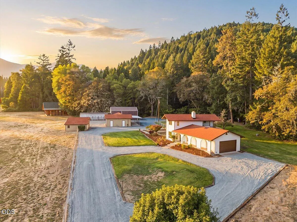 The finished Fish Hatchery property in warm evening light, with the house, outbuildings, open ground, and wooded hills