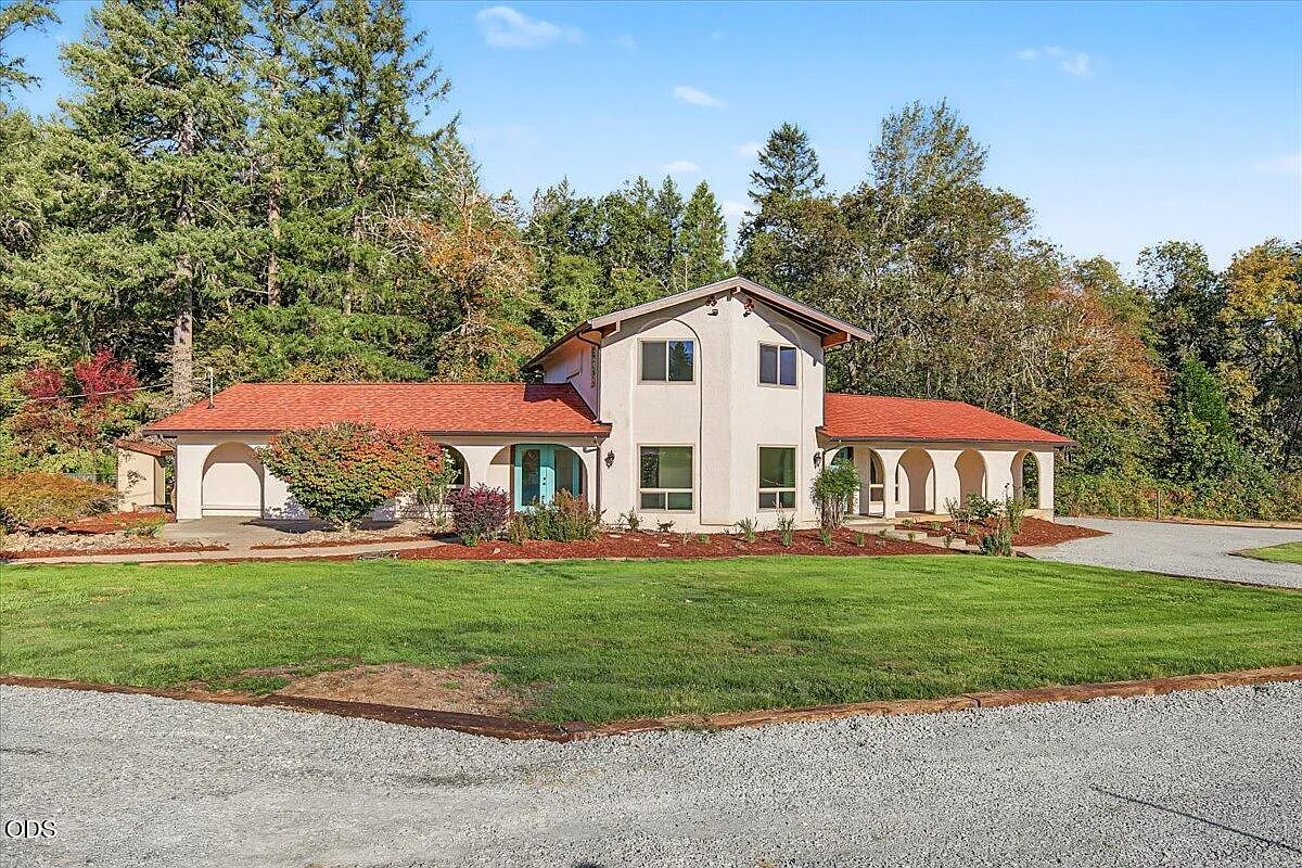 The finished house with its front arches exposed, trimmed planting, lawn, and gravel approach