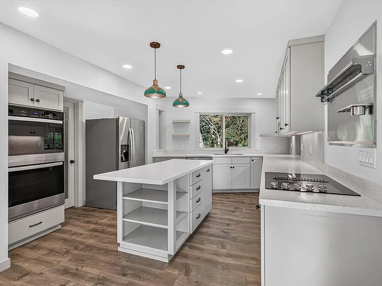 The finished kitchen with white cabinetry, stone counters, pendant lights, and an uncluttered island
