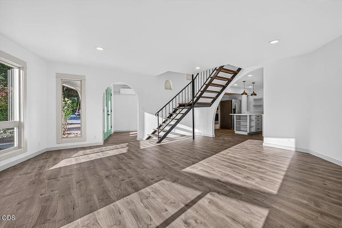 The finished living room with an open staircase, white walls, and continuous wood-look flooring