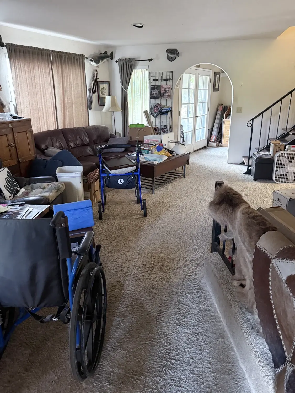 The living room with furniture and belongings across the carpet, beside the staircase and arched doorway