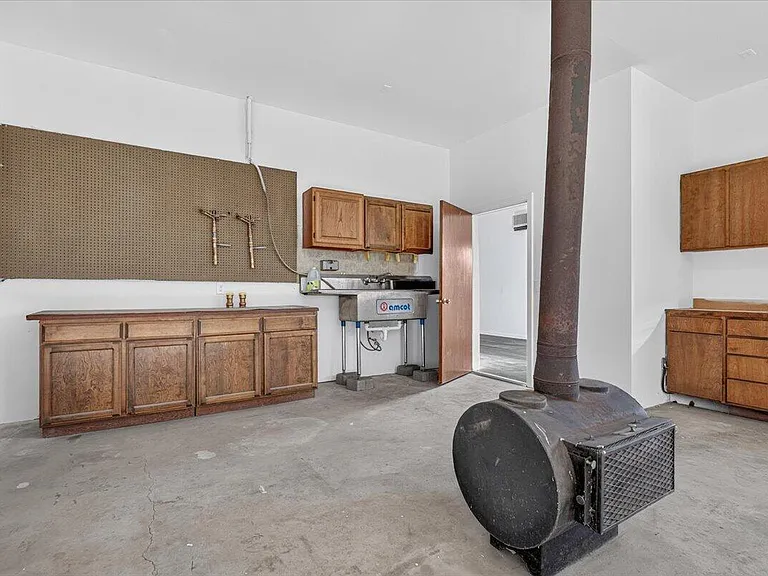 The cleared workshop, with the same barrel stove, wood cabinets, pegboard, and utility sink