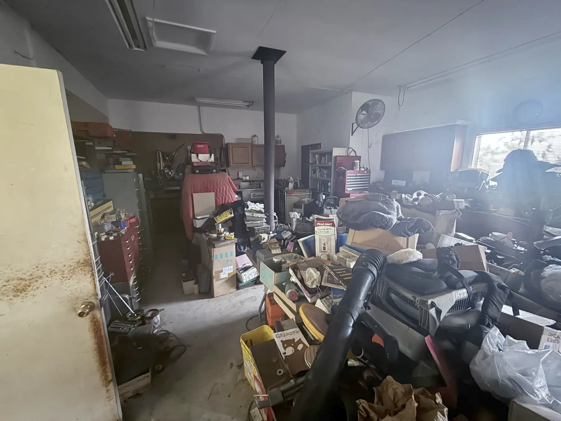 The workshop filled with stored items around a barrel stove, sink, and wood cabinets